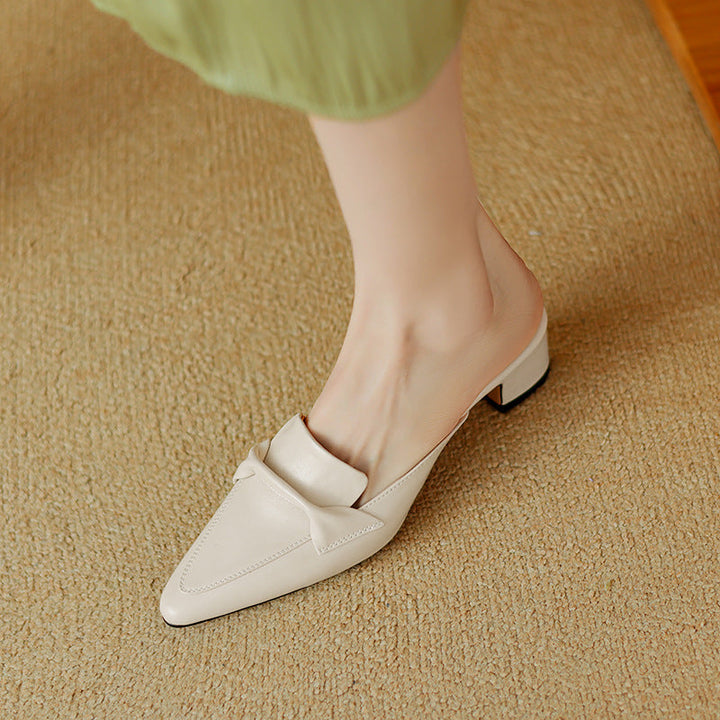 Top-down view of white leather slip-on mules with a classic bow, perfect elegant footwear