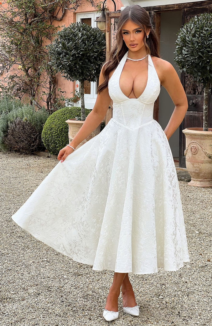 Chic white halter midi wedding guest dress with corset bodice and A-line skirt for a party or cocktail.
