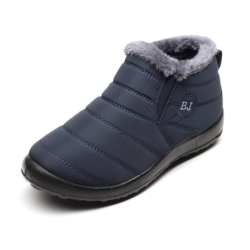A man wearing black waterproof snow boots, walking outdoors in a snowy environment. Practical winter footwear.