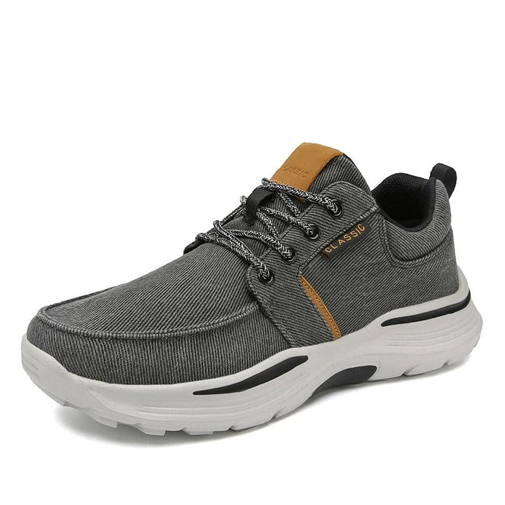 Stack of men's canvas comfort sneakers (khaki, gray, blue) displaying color options and design.