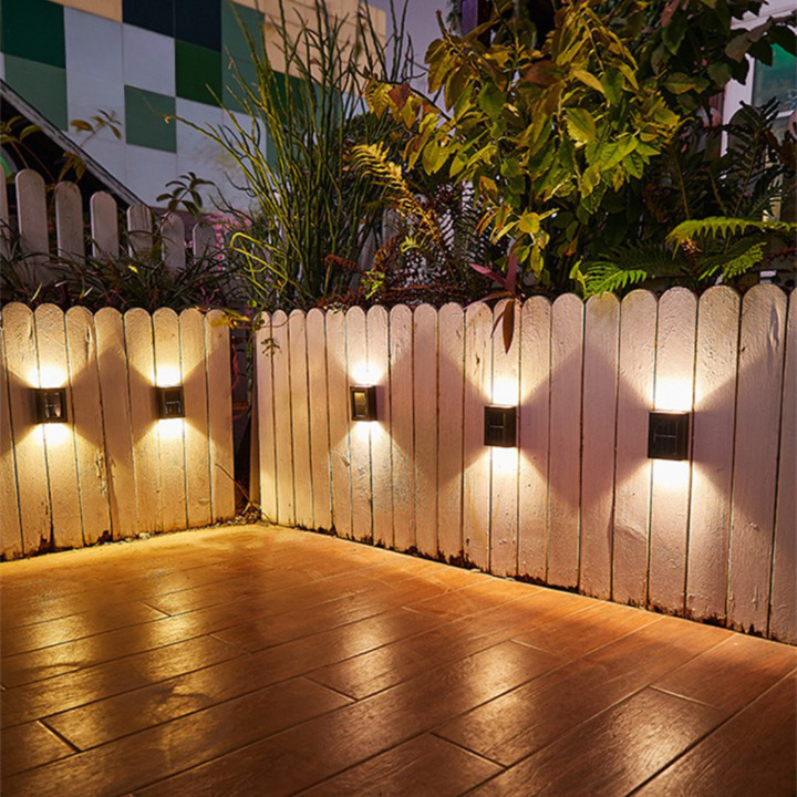 Wireless solar LED wall light mounted on a garden fence, illuminating a pathway. Easy exterior lighting solution.
