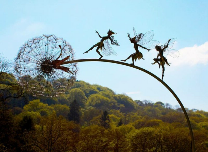 Whimsical metal fairy with lifelike dandelion stakes, ideal for enchanting garden decor, adding magic to outdoor spaces.