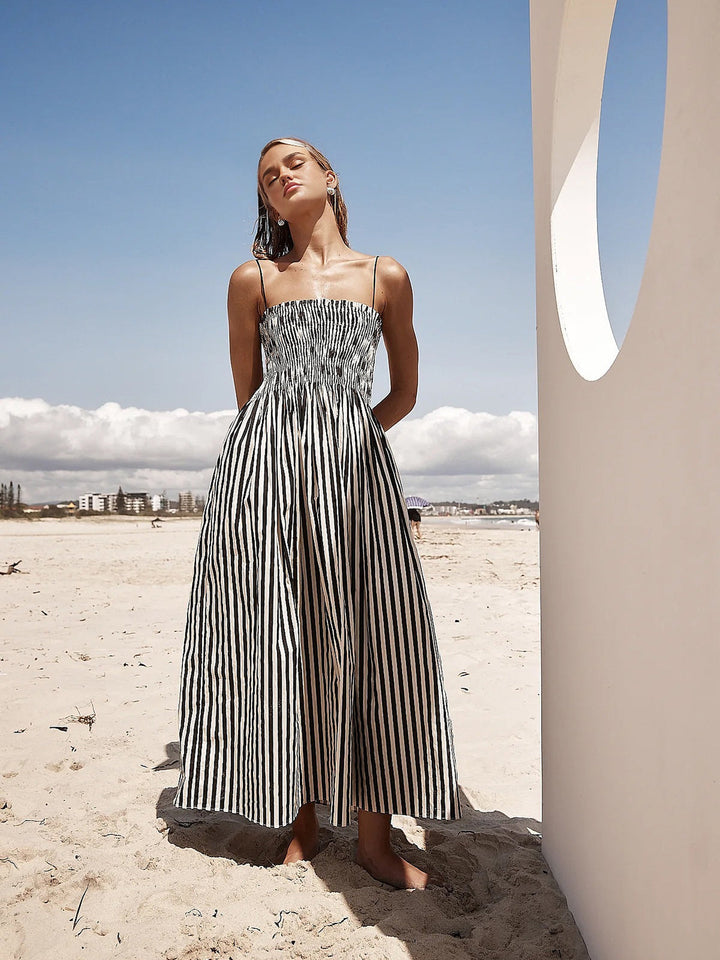 Women's elegant pinstripe smocked maxi dress in black, featuring a flowing A-line skirt and thin straps.