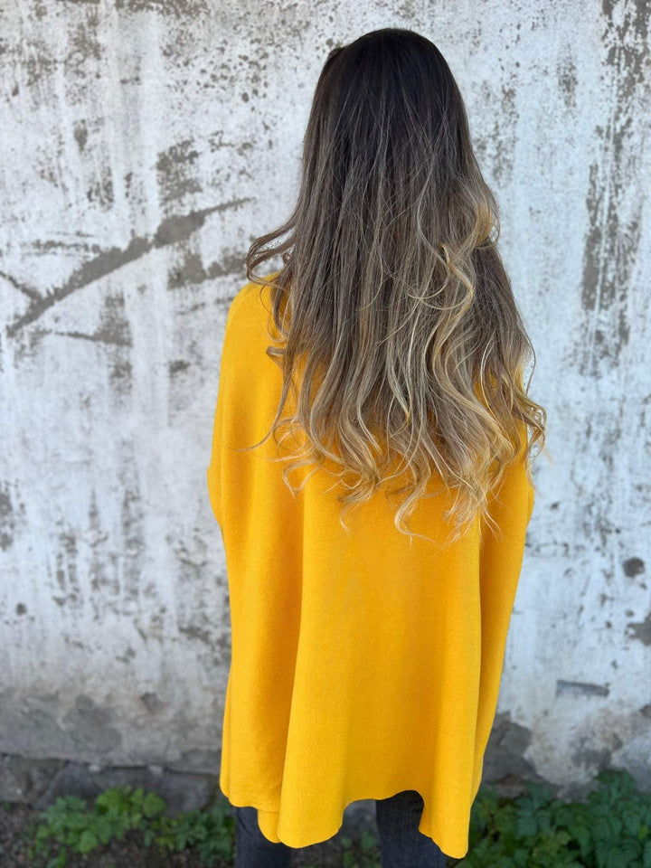 Side view of a women's long V-neck tunic sweater, showing its relaxed swing fit and comfortable pullover design.
