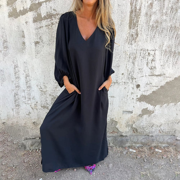 Full-length view of a women's elegant flowy maxi dress, complete with V-neck, pockets & balloon sleeves.