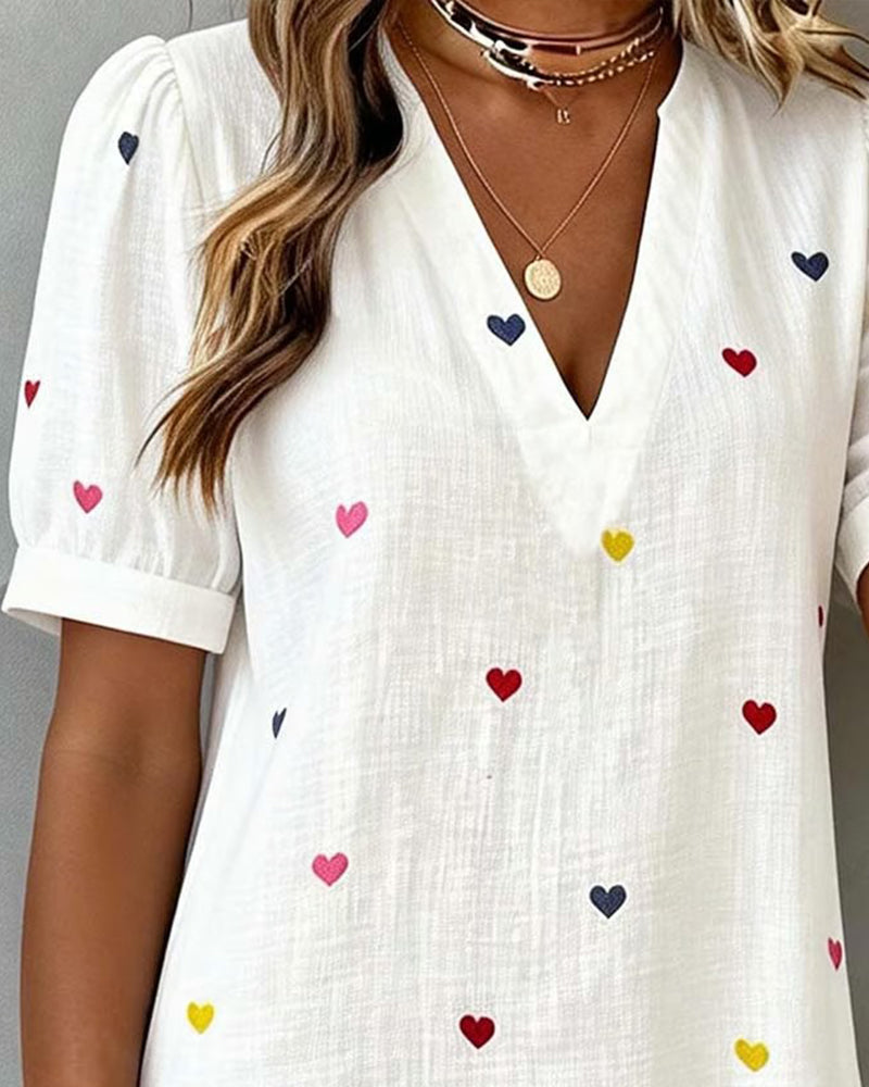 Charming women's mini dress featuring a vibrant heart print, V-neck, and trendy puff sleeves. Relaxed fit.
