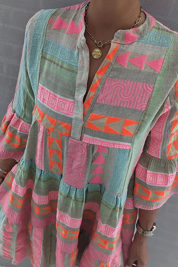 Elegant women's pink tiered mini dress with geometric print, V-neck, and stylish 3/4 sleeves. Casual spring fashion.