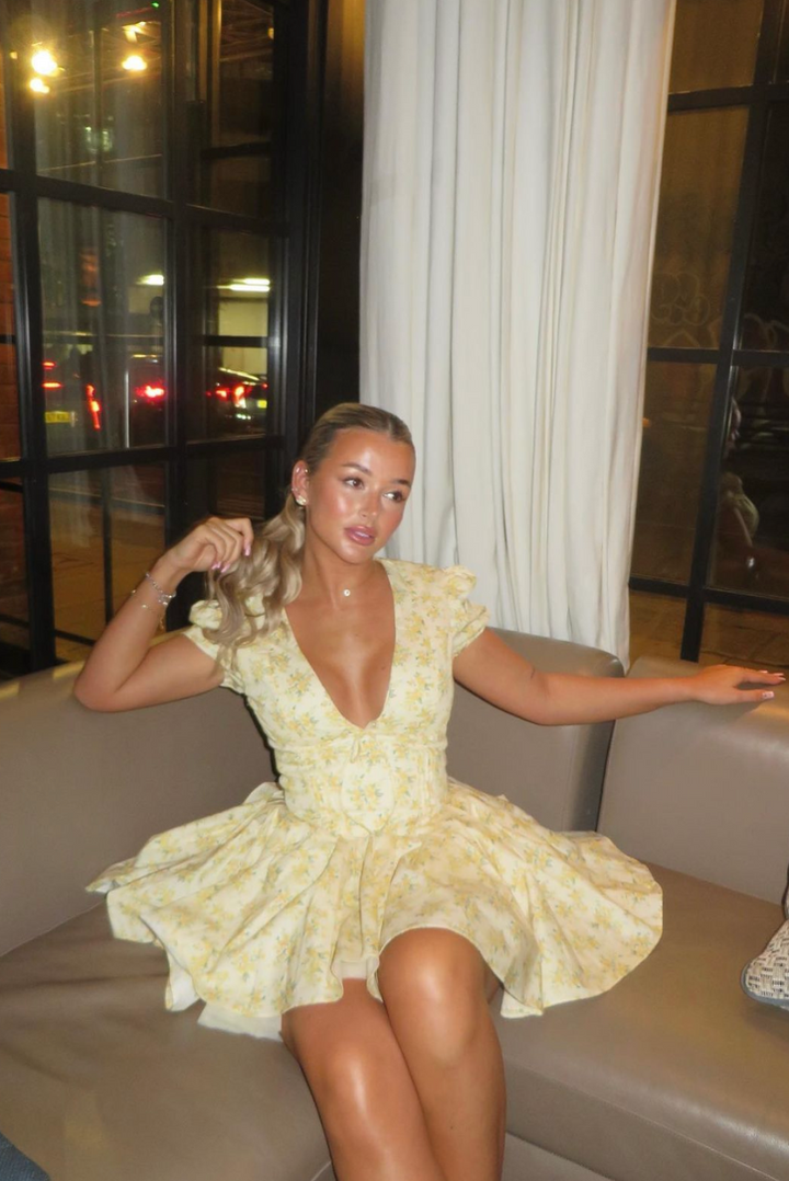 Casual women's floral A-line mini dress in yellow, featuring puff sleeves & an open back. Comfortable summer wear.